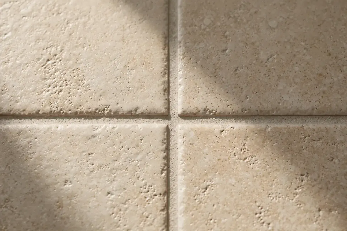 Corner of four beige porcelain tiles meeting at a clean grout line