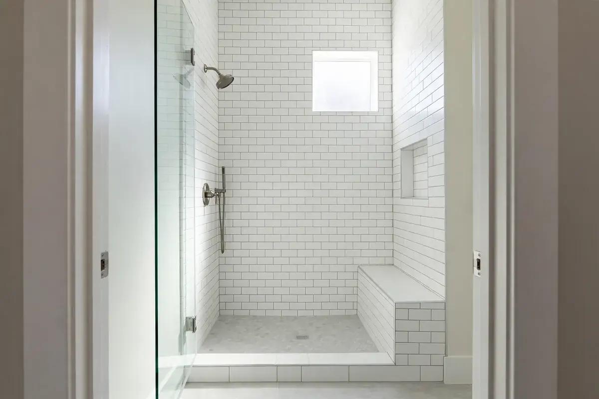 Tiled walk-in shower with white wall tile and a small window letting in light